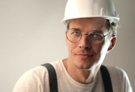 Safety Construction Vest - Content male builder in workwear and hardhat smiling on gray background in studio and looking at camera