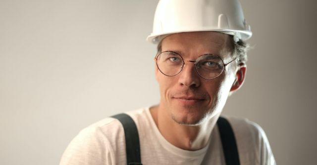 Safety Construction Vest - Content male builder in workwear and hardhat smiling on gray background in studio and looking at camera