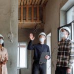 Hard Hats - A Group of People Standing Inside the House Talking while Wearing Face Masks and Hard Hats