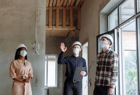 Hard Hats - A Group of People Standing Inside the House Talking while Wearing Face Masks and Hard Hats