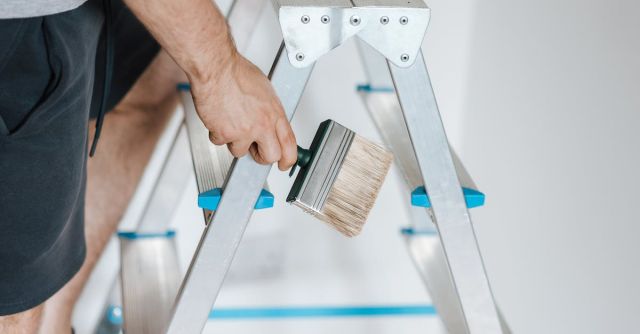 Builder - Painter with brush climbing ladder during renovation work