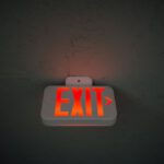 Construction Industry - From below of illuminated exit sign hanging on gray concrete ceiling in dark room
