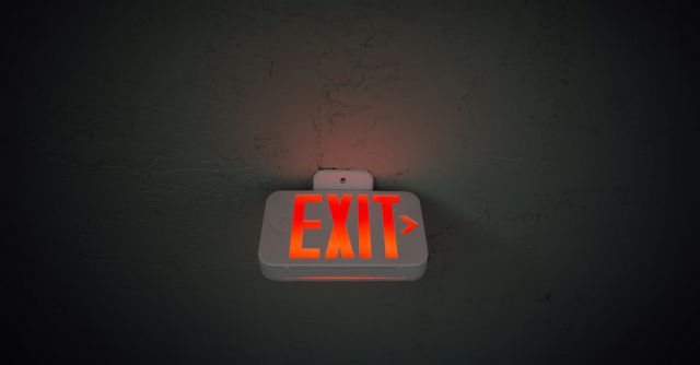 Construction Industry - From below of illuminated exit sign hanging on gray concrete ceiling in dark room