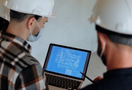 Hard Hats - People in Hard Hats Looking at a Blueprint on a Laptop