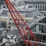 Construction - Aerial view of red tower crane between multistory buildings and glass skyscrapers on cloudy day in London