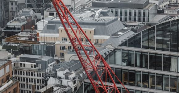 Construction - Aerial view of red tower crane between multistory buildings and glass skyscrapers on cloudy day in London