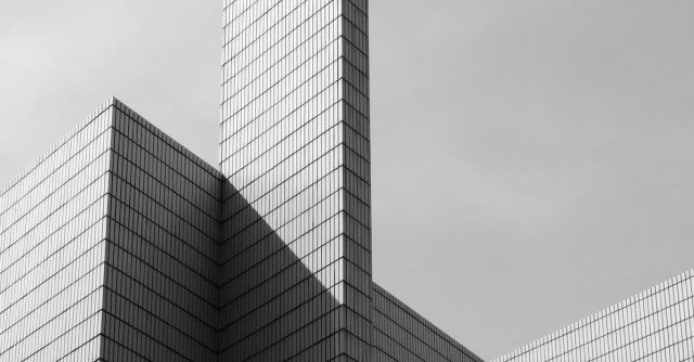 Skyscraper Construction - From below black and white of contemporary geometric construction exterior with tall walls under light cloudy sky in sunny day