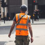 Safety Construction Vest - Back view of unrecognizable young male constructor in protective helmet and vest walking on asphalt road in modern city district