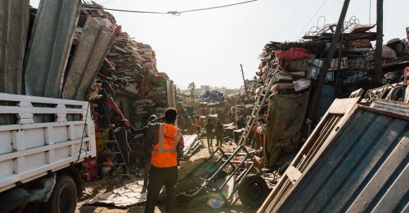 Loader - Unrecognizable workmen standing near pile of metal scrap in dump