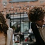 Brick Building - Woman in Beige Coat Standing Beside Man in Black Suit