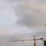 Industrial Hoist - Bright high cranes near urban house during construction under cloudy sky in daylight