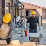 Construction Workers - Man in Black Shirt Wearing Yellow Hard Hat Pushing Barrow