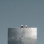 Construction - From below of anonymous distant engineers in helmets working on rooftop of modern skyscraper with glass mirrored walls against cloudless blue sky