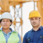 Construction Workers - A Man and a Woman Wearing Hardhats Standing Near a Metal Structure