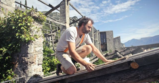Builder - Focused man building roof of wooden construction