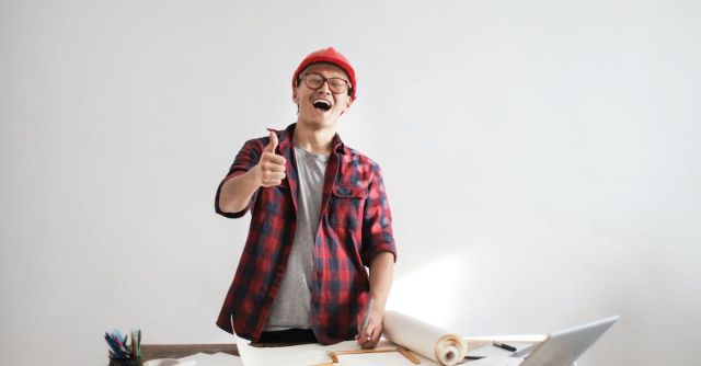 Builder - Laughing male constructor showing thumb up at working desk